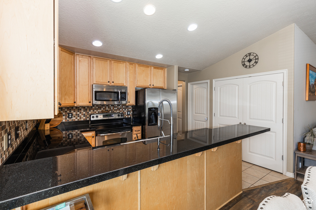 Kitchen with stainless steel appliances, a peninsula, backsplash, light brown cabinets, and a kitchen bar
