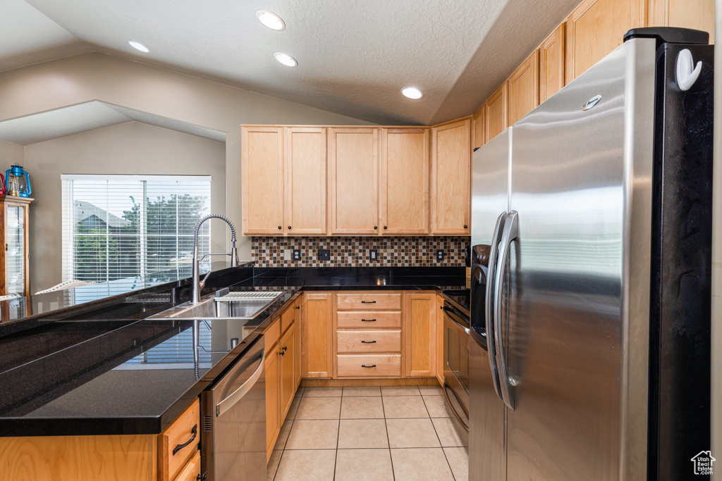 Kitchen featuring stainless steel appliances, a sink, light brown cabinets, vaulted ceiling, and light tile patterned floors