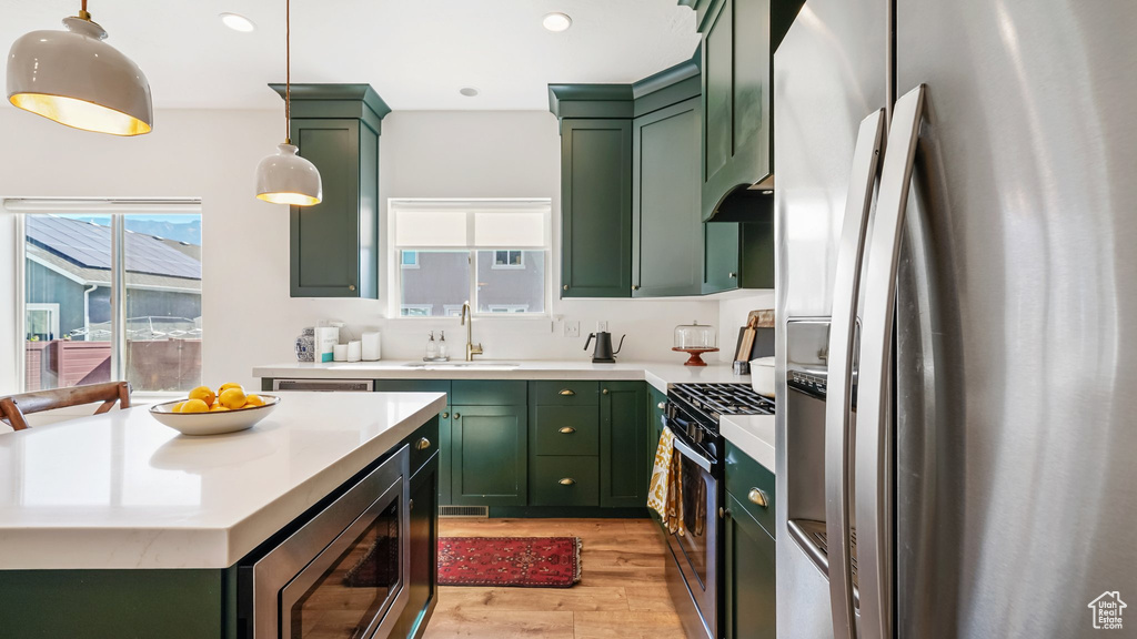 Kitchen featuring green cabinetry, stainless steel appliances, light wood finished floors, light countertops, and recessed lighting