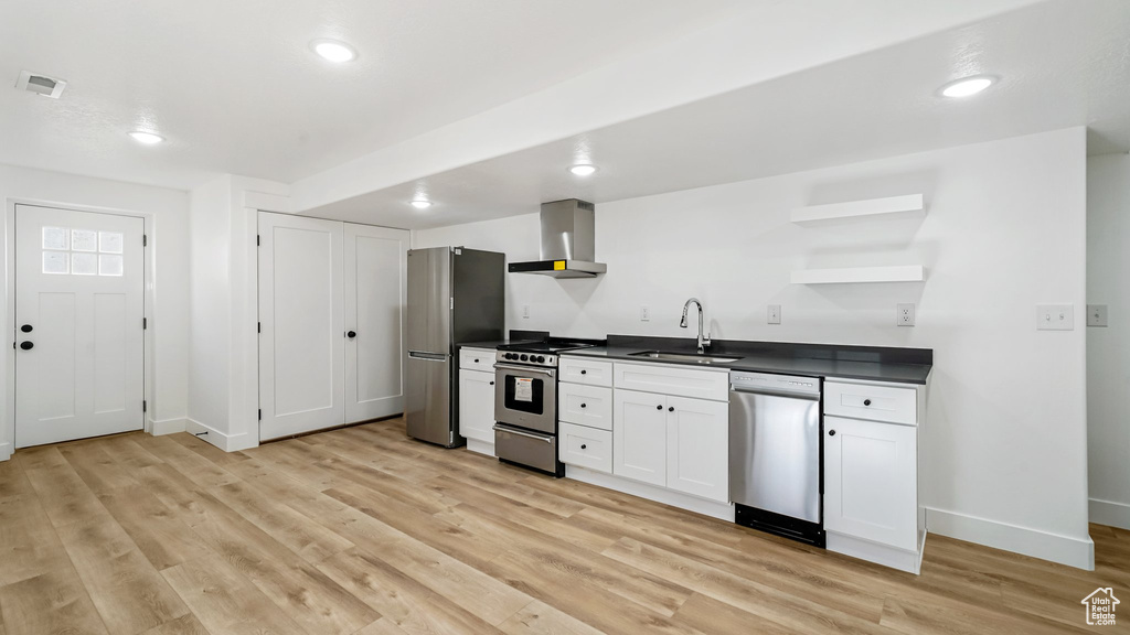 Kitchen with stainless steel appliances, wall chimney exhaust hood, open shelves, dark countertops, and light wood-type flooring