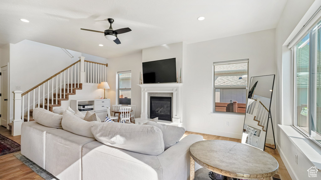 Living room featuring stairway, a glass covered fireplace, ceiling fan, light wood-style floors, and recessed lighting