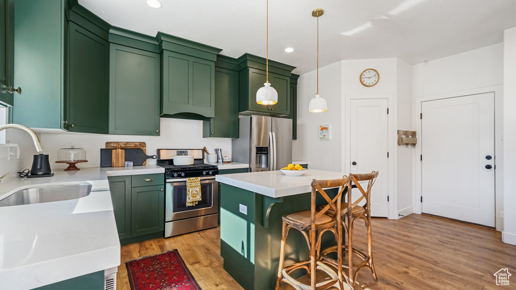Kitchen with green cabinetry, appliances with stainless steel finishes, light countertops, a kitchen breakfast bar, and recessed lighting