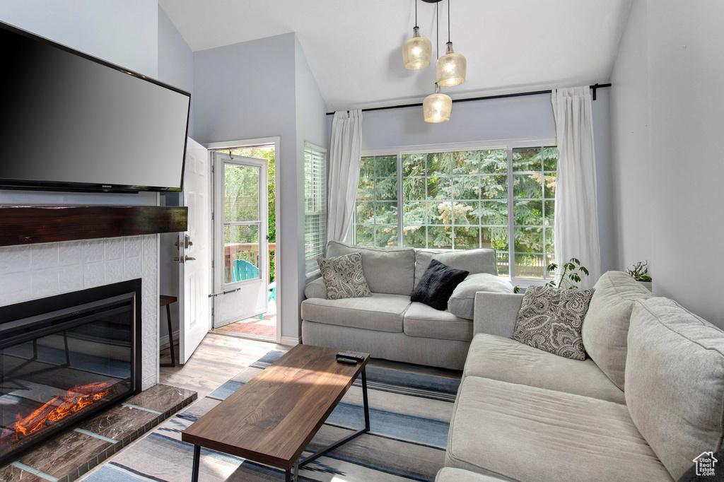 Living area featuring a tiled fireplace, vaulted ceiling, and wood finished floors