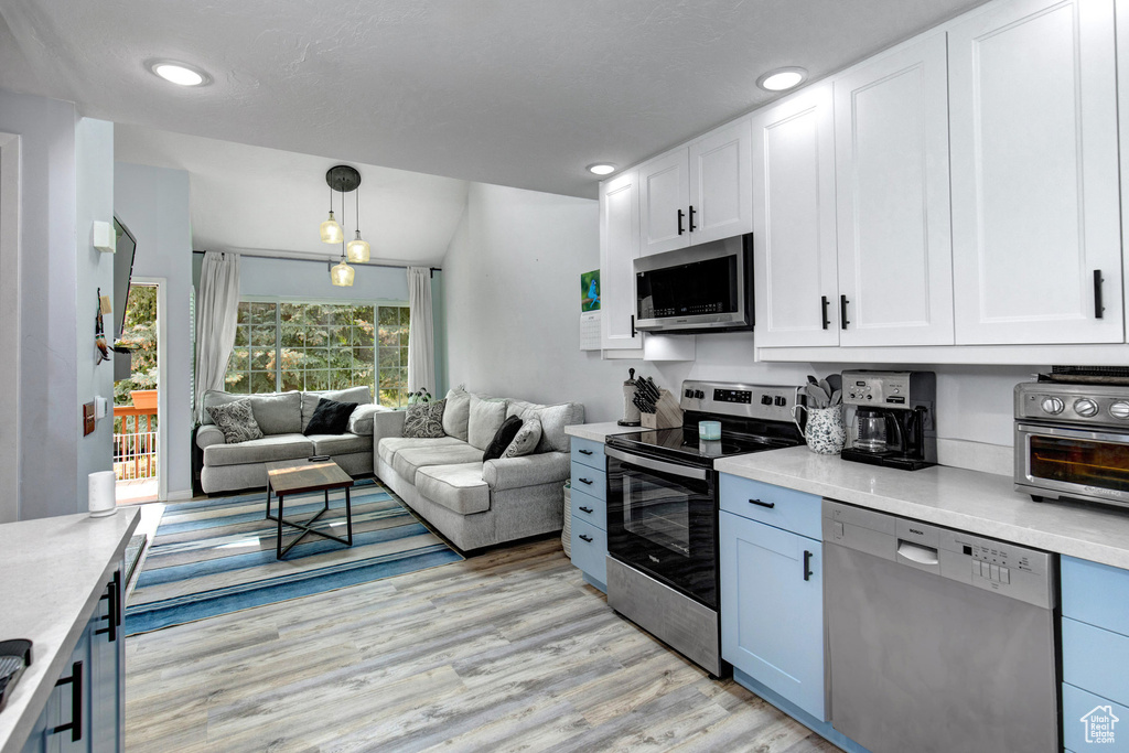 Kitchen with stainless steel appliances, open floor plan, light wood-style flooring, light countertops, and recessed lighting