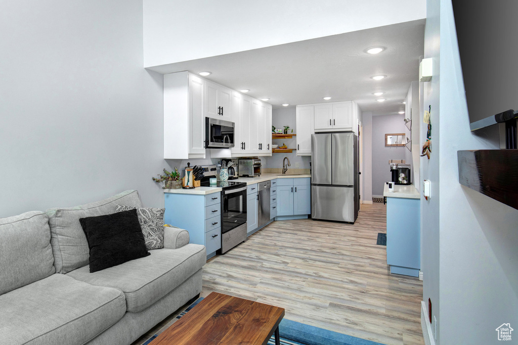 Kitchen with appliances with stainless steel finishes, open floor plan, open shelves, light wood-style floors, and light countertops