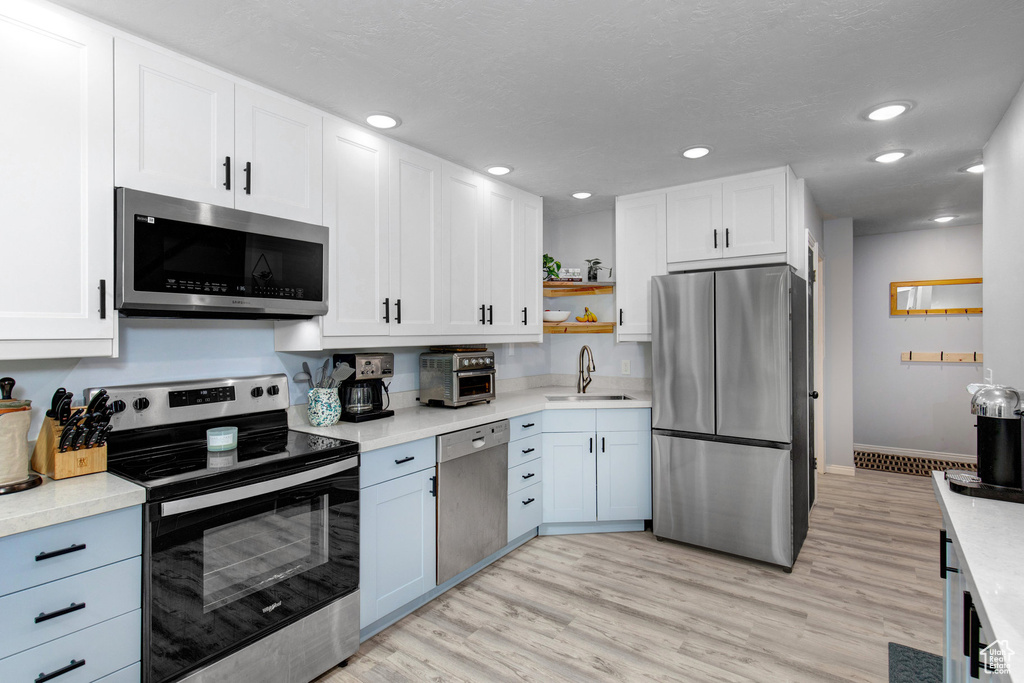 Kitchen featuring appliances with stainless steel finishes, open shelves, white cabinets, light countertops, and recessed lighting