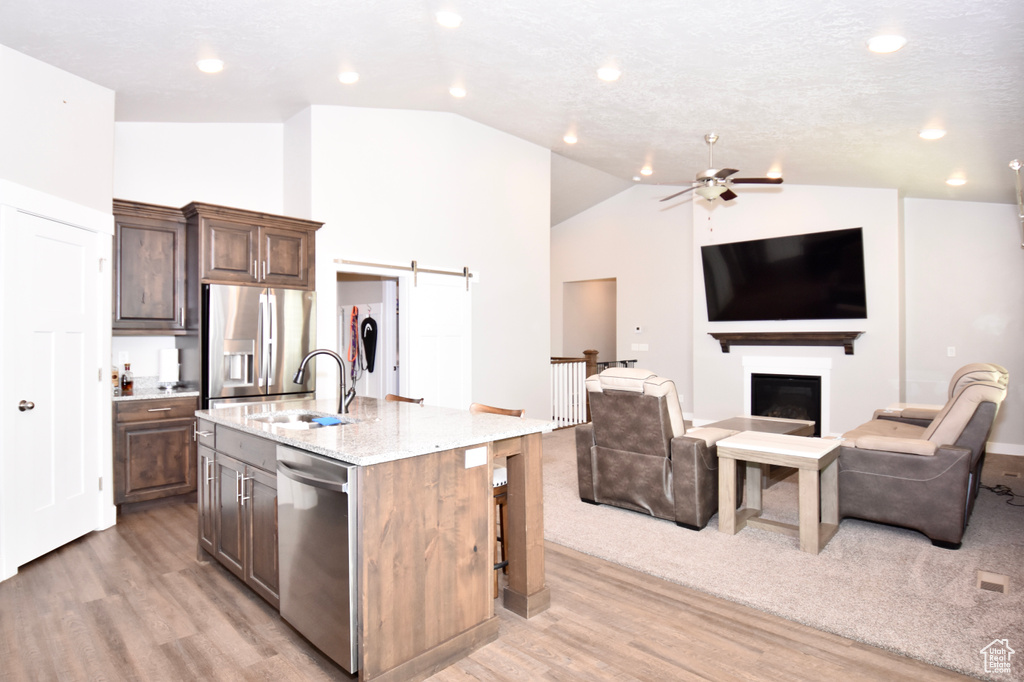Kitchen featuring stainless steel appliances, a sink, light wood-style flooring, lofted ceiling, and open floor plan