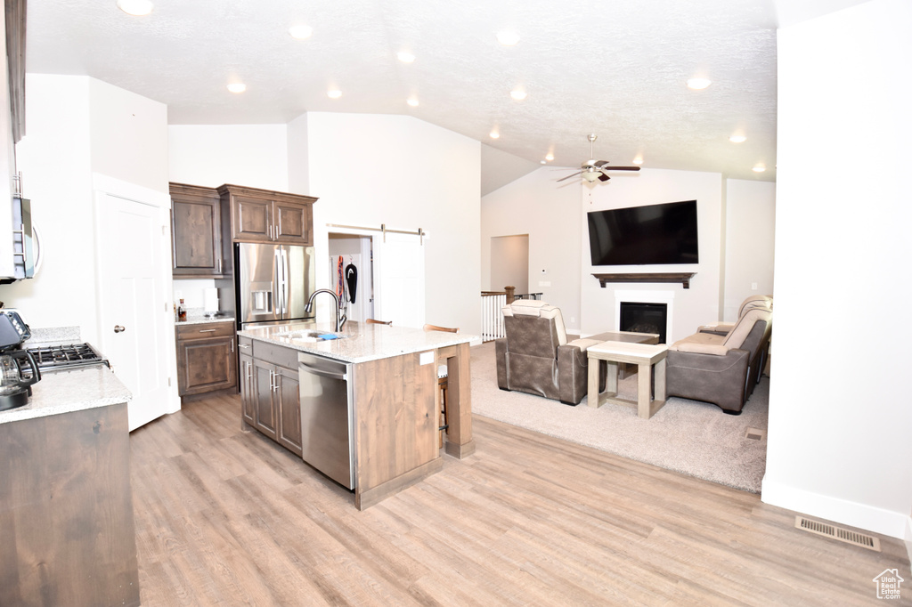 Kitchen with appliances with stainless steel finishes, open floor plan, light wood-style flooring, a ceiling fan, and vaulted ceiling