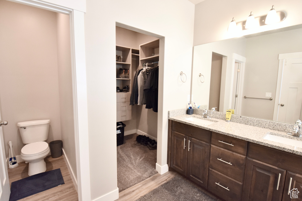 Bathroom with double vanity, toilet, wood finished floors, baseboards, and a spacious closet