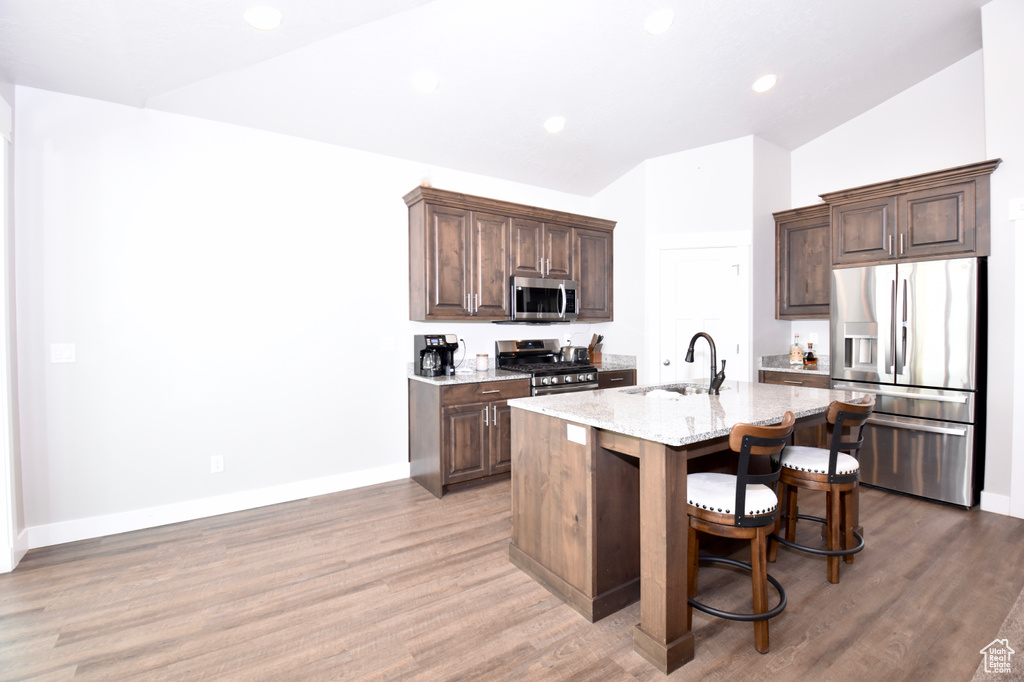 Kitchen with stainless steel appliances, a sink, vaulted ceiling, a center island with sink, and light stone countertops