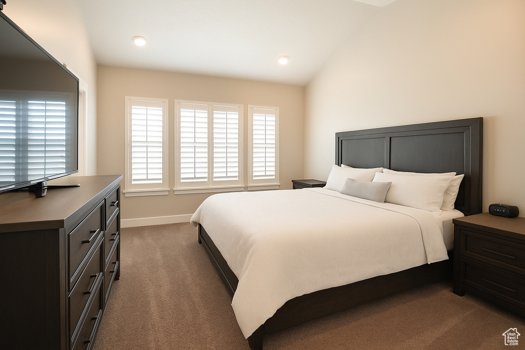 Bedroom with multiple windows, dark carpet, baseboards, and vaulted ceiling