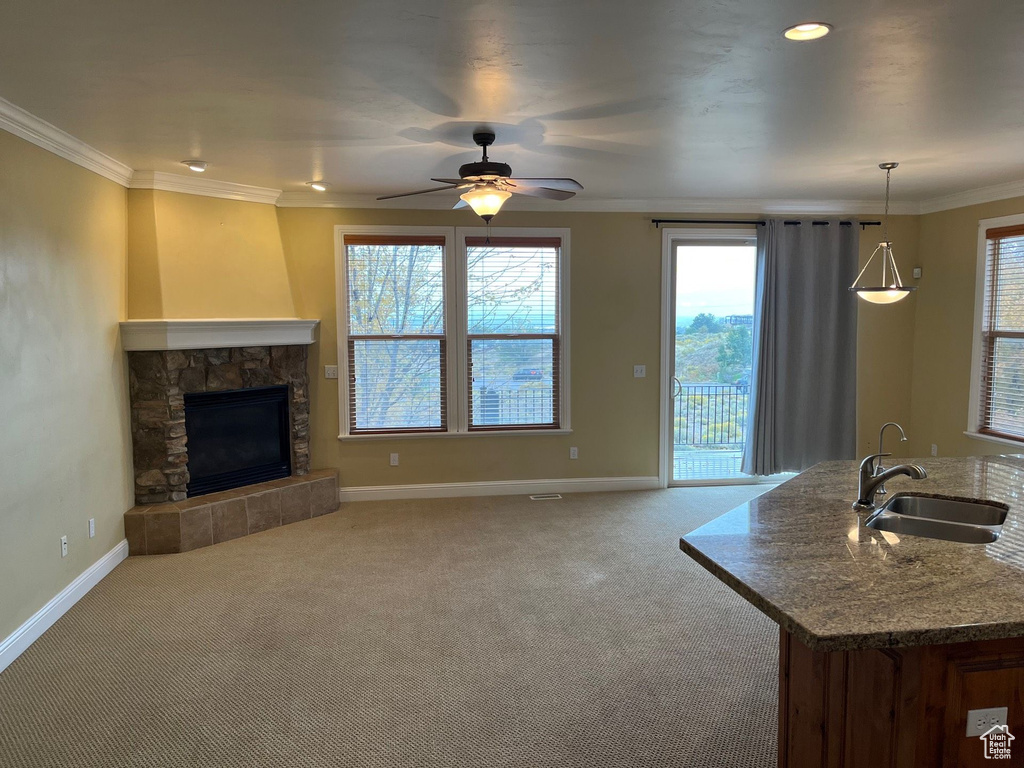 Unfurnished living room with carpet, ceiling fan, ornamental molding, and a fireplace with raised hearth
