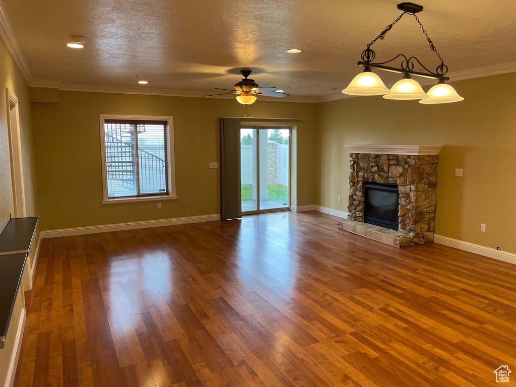 Unfurnished living room featuring wood finished floors, a ceiling fan, a stone fireplace, and crown molding
