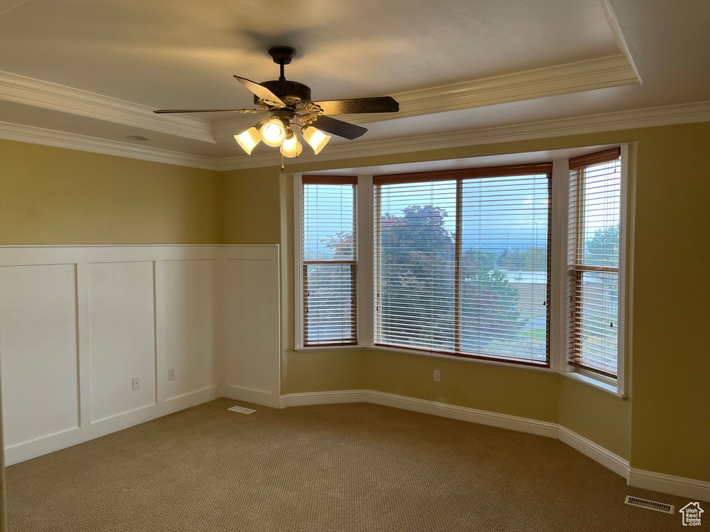 Empty room featuring a raised ceiling, ornamental molding, healthy amount of natural light, ceiling fan, and light carpet