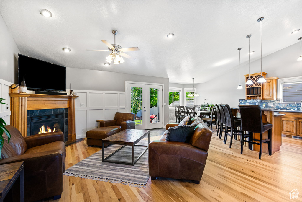 Living area featuring light wood-type flooring, a ceiling fan, a tile fireplace, a decorative wall, and vaulted ceiling