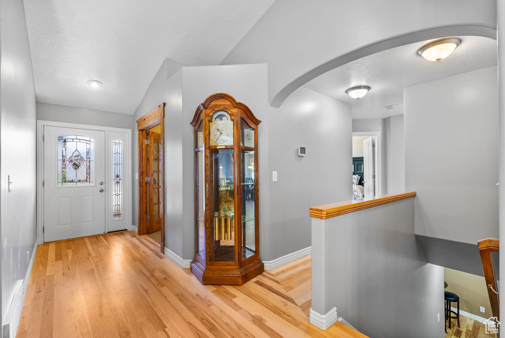 Entrance foyer with arched walkways, light wood finished floors, and lofted ceiling