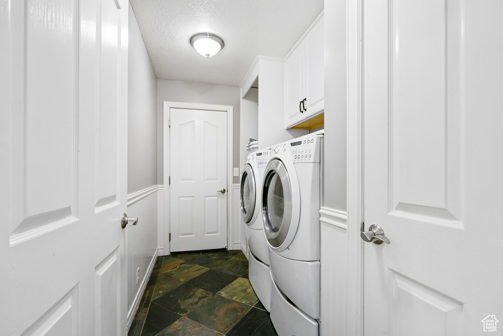 Laundry area featuring washer and dryer, dark stone finish flooring, and cabinet space