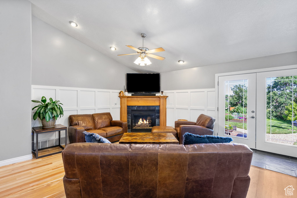 Living area with a decorative wall, a tiled fireplace, a ceiling fan, light wood finished floors, and wainscoting