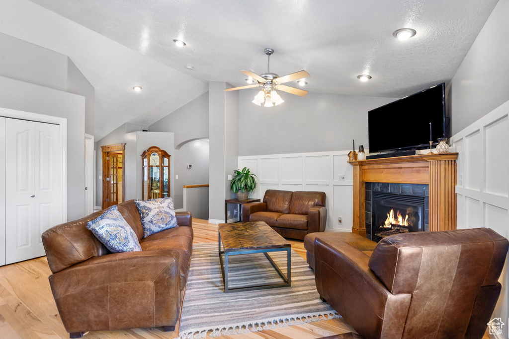 Living area featuring lofted ceiling, a tiled fireplace, a decorative wall, wood finished floors, and a ceiling fan