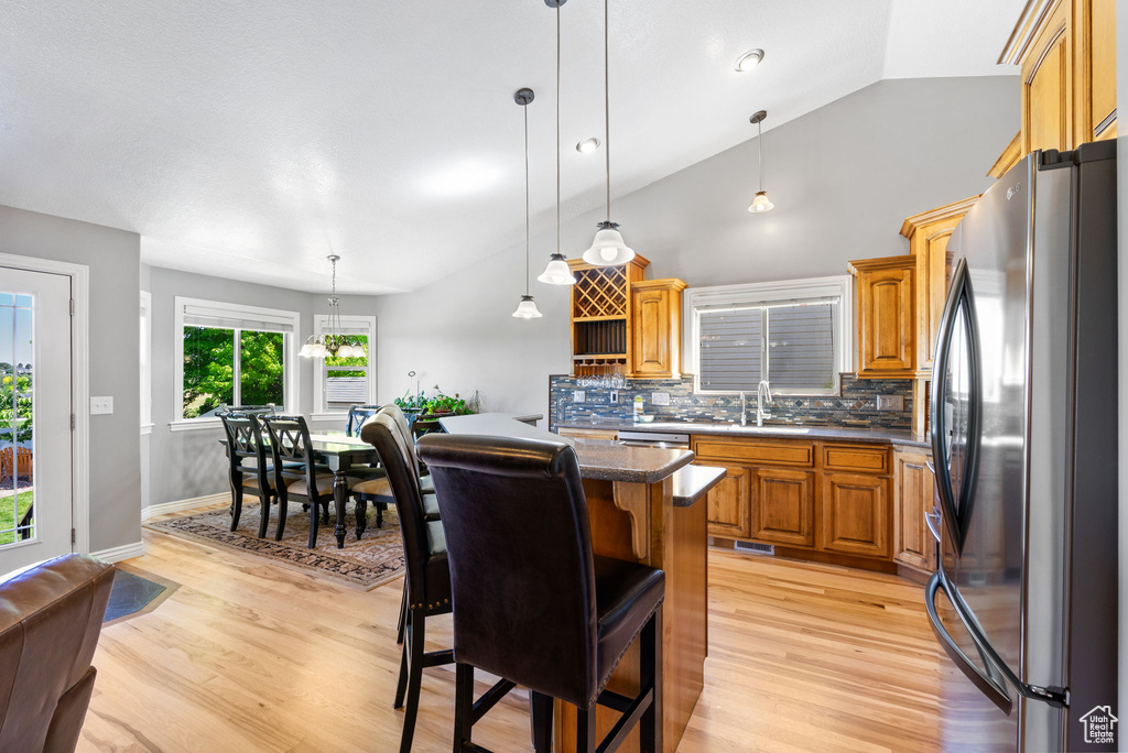 Kitchen featuring freestanding refrigerator, decorative backsplash, light wood-type flooring, a kitchen bar, and lofted ceiling
