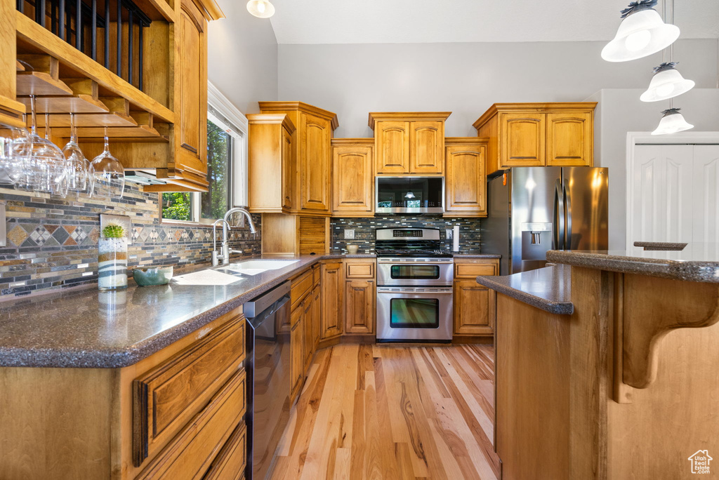 Kitchen featuring stainless steel appliances, light wood-type flooring, brown cabinets, hanging light fixtures, and backsplash