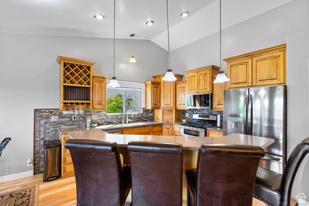 Kitchen with stainless steel appliances, tasteful backsplash, a kitchen breakfast bar, high vaulted ceiling, and light wood finished floors
