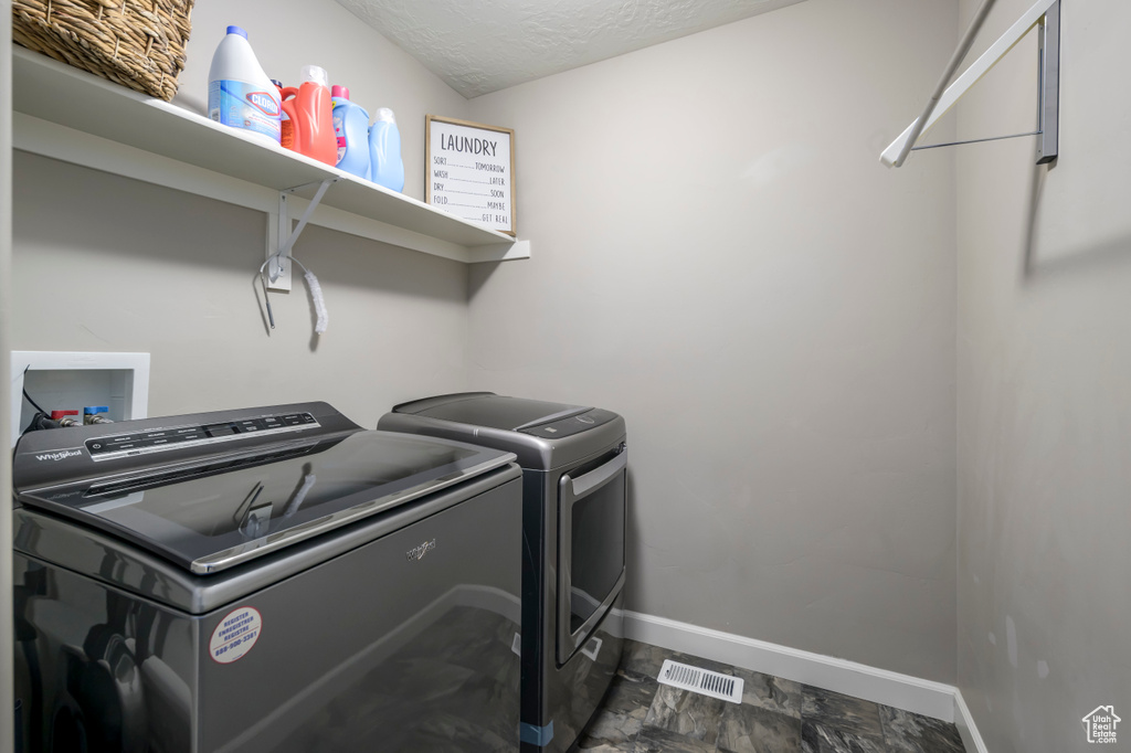 Laundry room featuring washing machine and clothes dryer, baseboards, and a textured ceiling