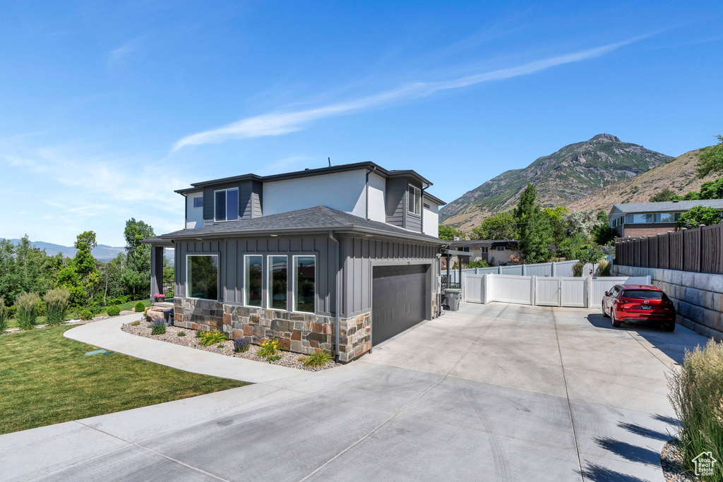 View of front of home featuring board and batten siding, a mountain view, concrete driveway, stone siding, and roof with shingles