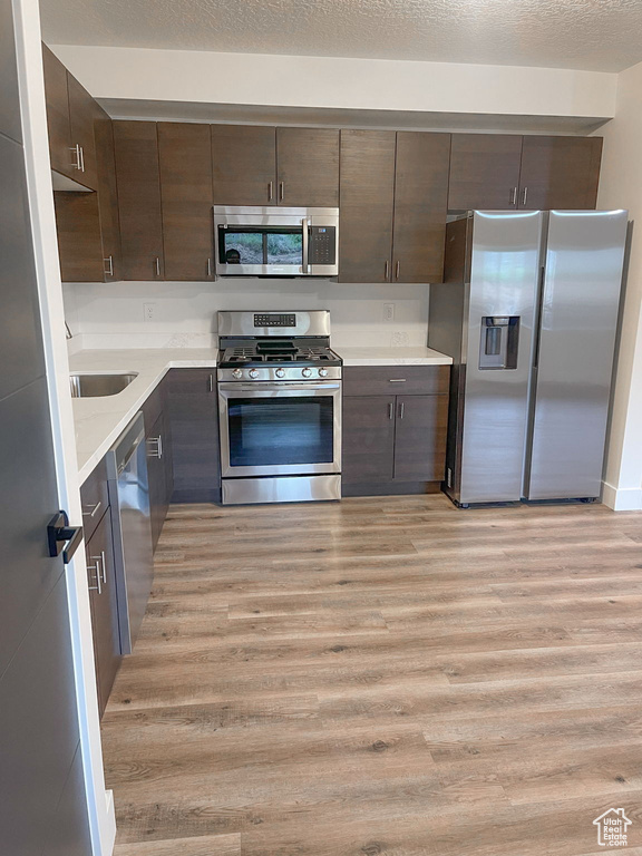 Kitchen with stainless steel appliances, light wood-style floors, dark brown cabinetry, and light countertops