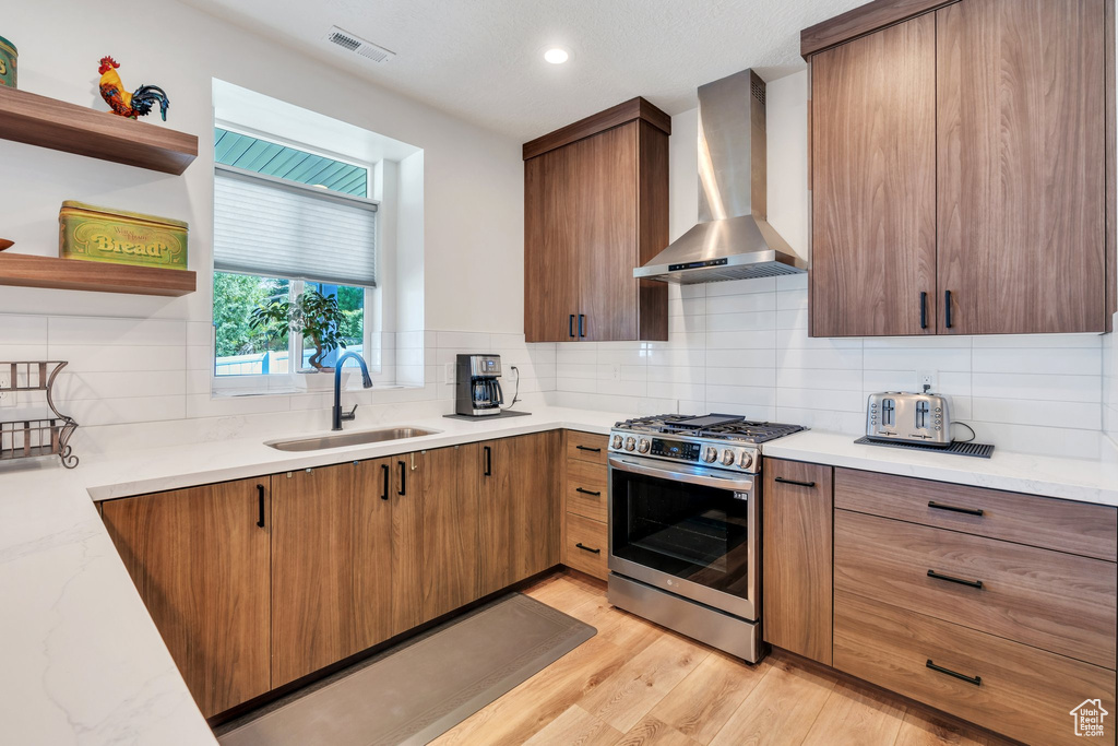 Kitchen with wall chimney exhaust hood, gas range, decorative backsplash, open shelves, and light wood-style flooring