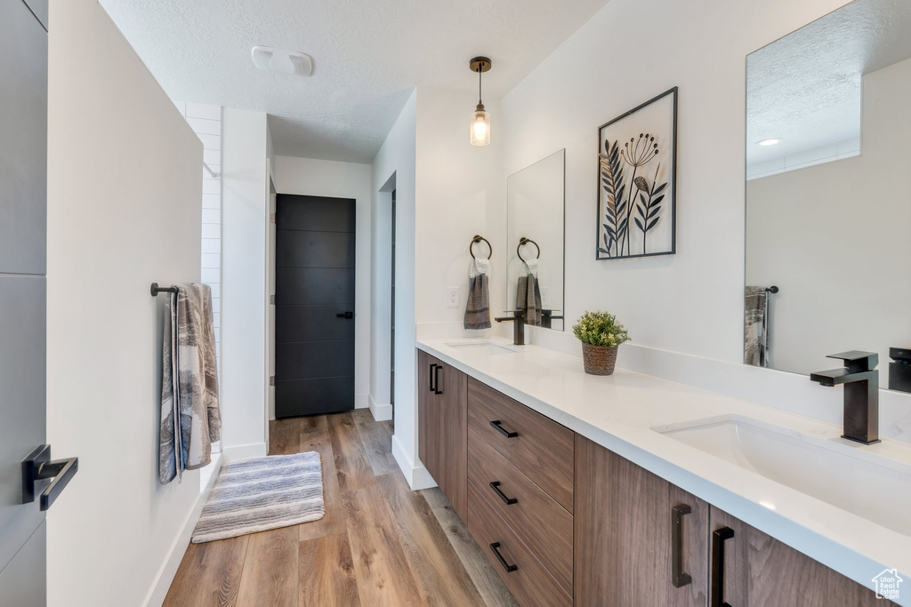 Bathroom with double vanity, wood finished floors, and a textured ceiling