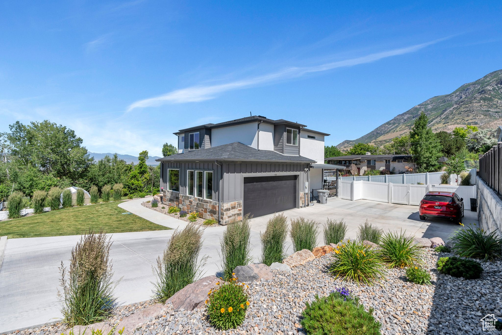 View of front facade with a mountain view, concrete driveway, board and batten siding, stone siding, and roof with shingles