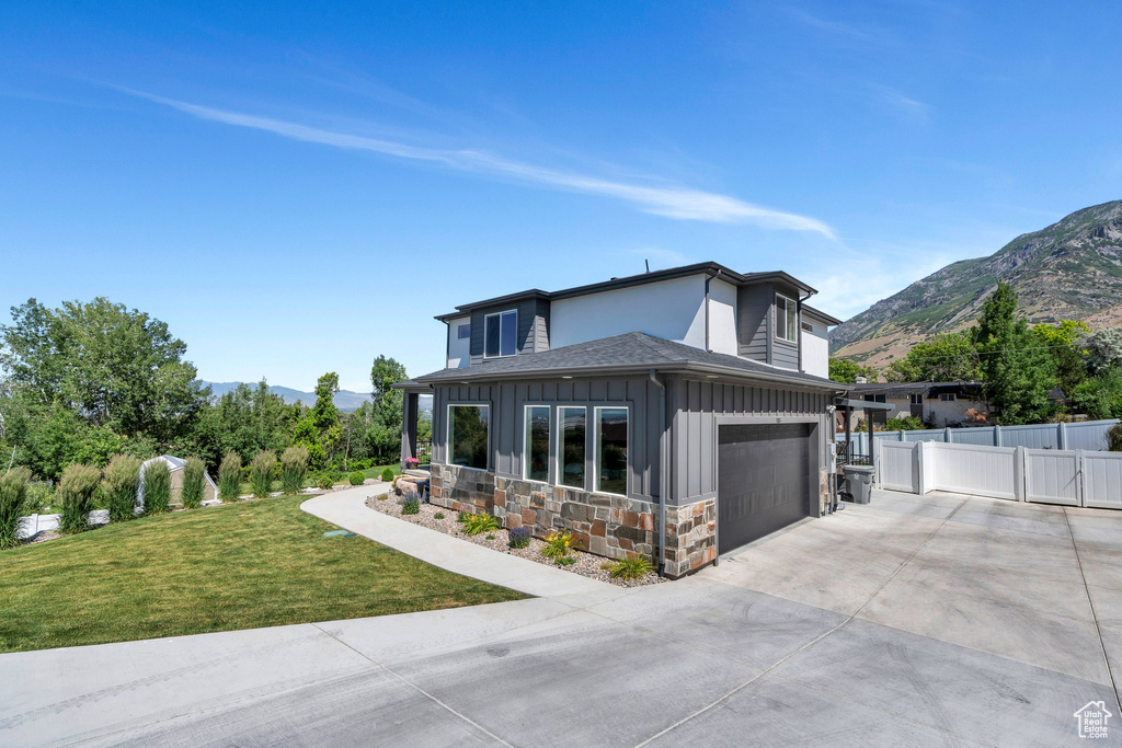 View of front of home with board and batten siding, concrete driveway, a mountain view, and roof with shingles