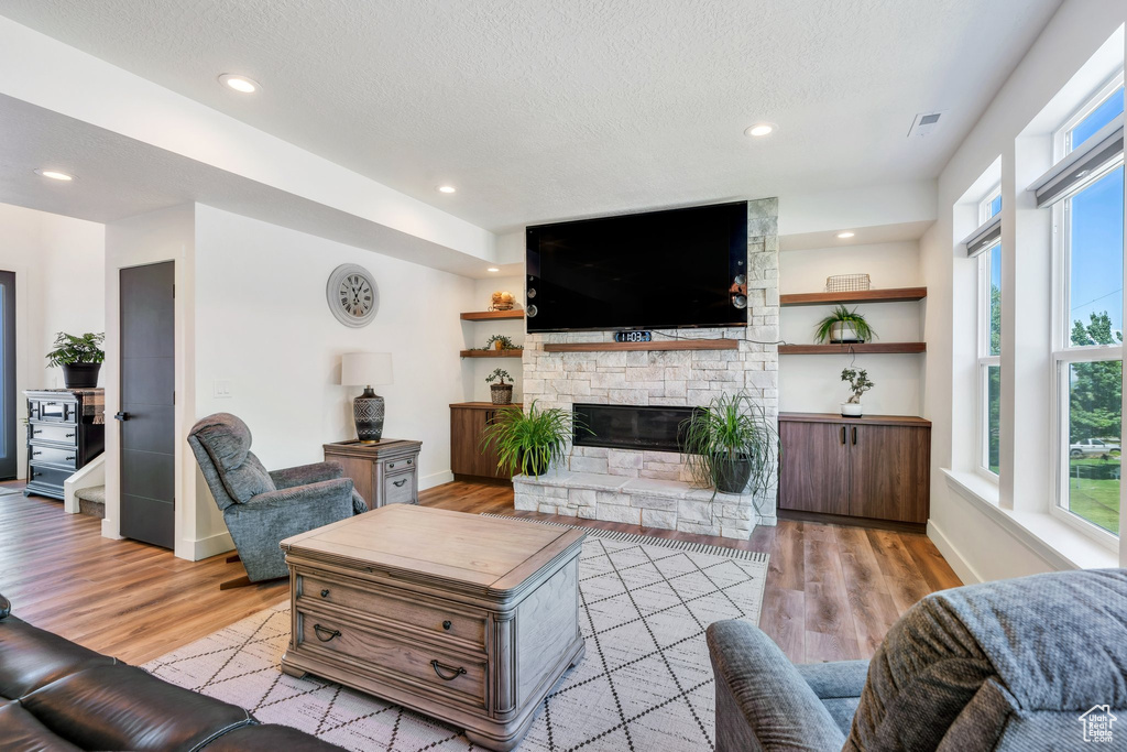 Living room with light wood finished floors, a fireplace, a textured ceiling, and recessed lighting