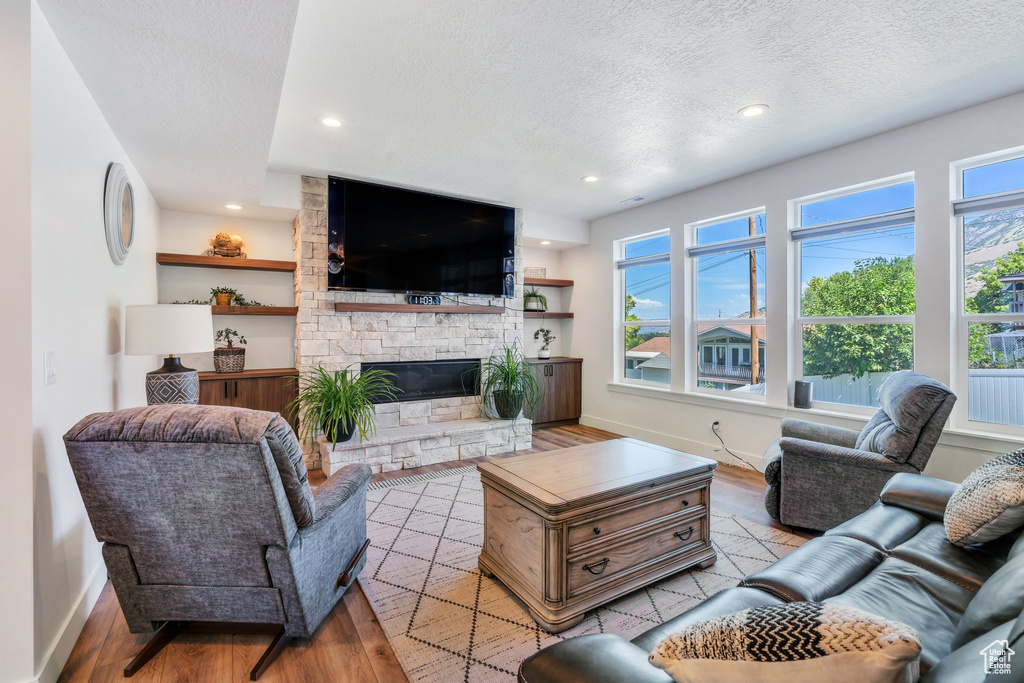 Living area featuring a textured ceiling, light wood-style flooring, a stone fireplace, and recessed lighting