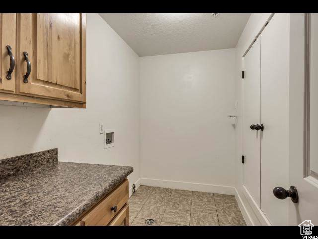 Laundry room with cabinet space, washer hookup, baseboards, a textured ceiling, and light tile patterned floors