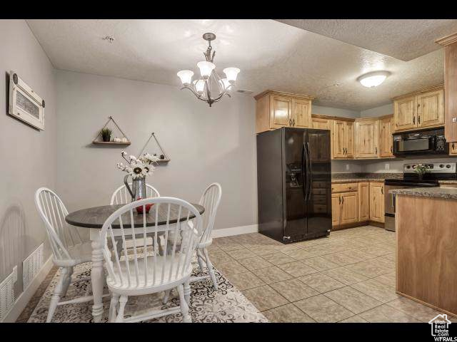 Kitchen with black appliances, baseboards, a chandelier, dark countertops, and light brown cabinetry