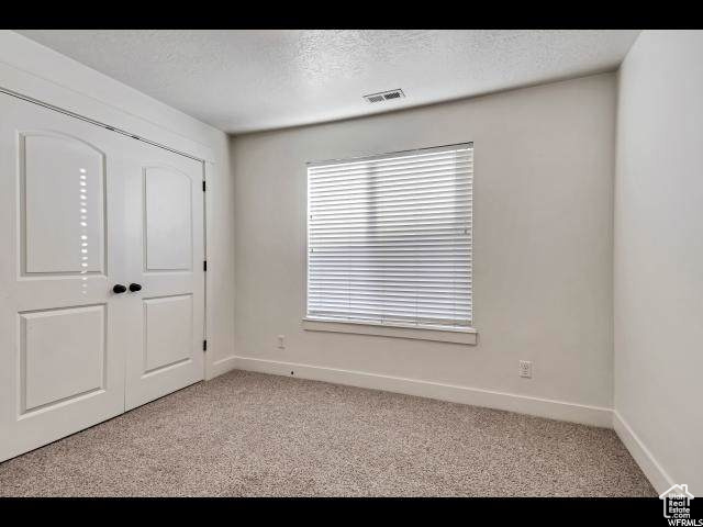 Unfurnished bedroom with light colored carpet, baseboards, a textured ceiling, and a closet
