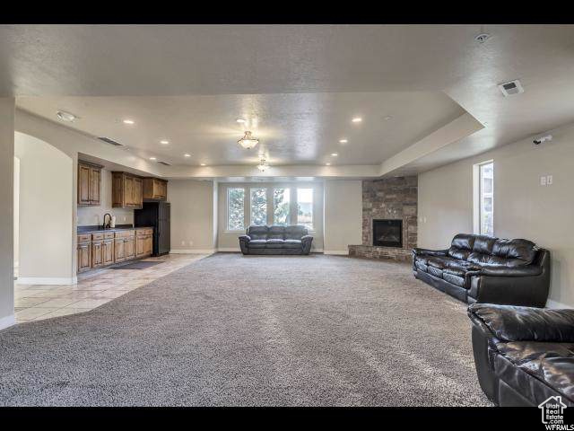 Living room with light colored carpet, baseboards, a stone fireplace, a raised ceiling, and recessed lighting