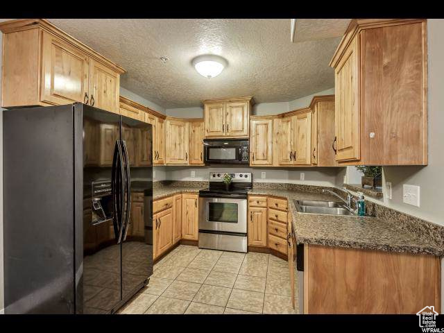 Kitchen featuring black appliances, a sink, a textured ceiling, light tile patterned floors, and dark countertops