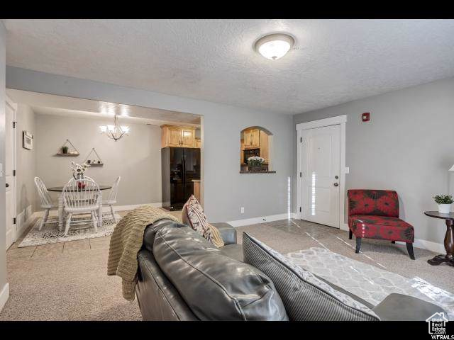 Living area with light carpet, baseboards, a chandelier, and a textured ceiling