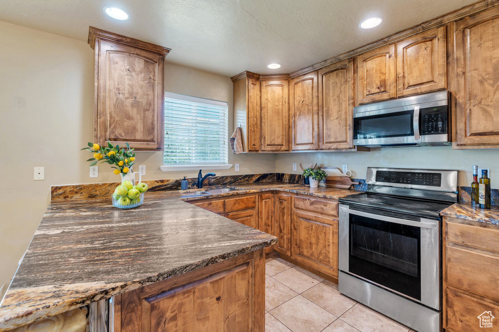 Kitchen featuring stainless steel appliances, recessed lighting, light tile patterned flooring, brown cabinetry, and dark stone counters