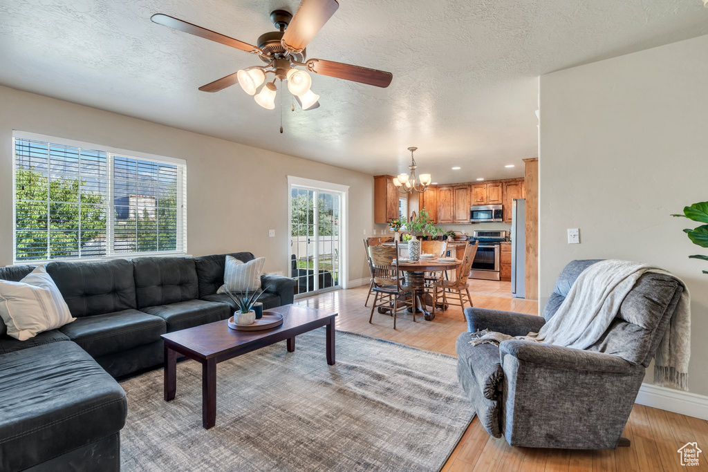 Living area with light wood-type flooring, a ceiling fan, a chandelier, a textured ceiling, and recessed lighting