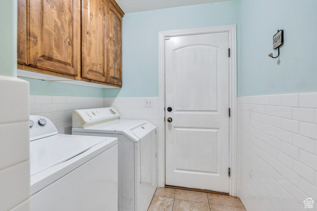 Laundry area featuring washing machine and clothes dryer, tile walls, cabinet space, a wainscoted wall, and light tile patterned flooring