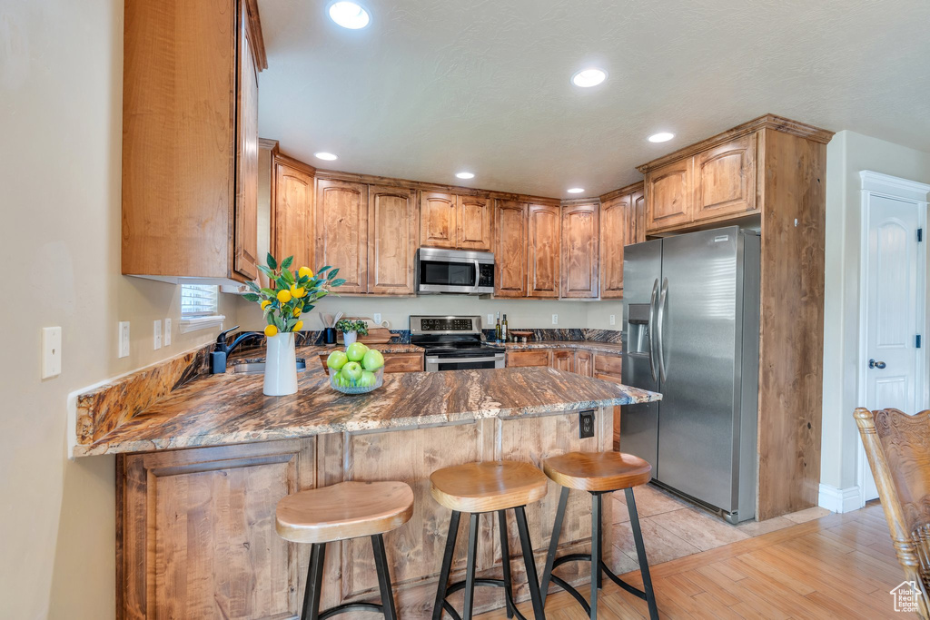 Kitchen with stainless steel appliances, a peninsula, light wood-style flooring, a breakfast bar, and recessed lighting