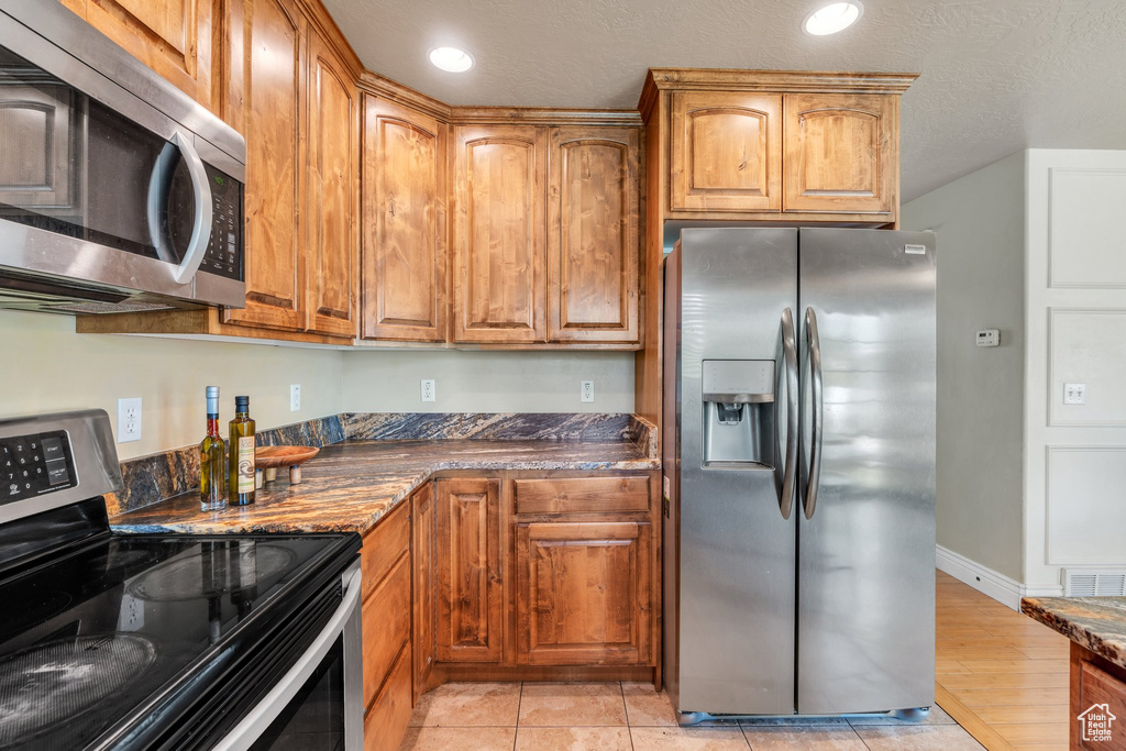 Kitchen featuring appliances with stainless steel finishes, brown cabinets, dark stone counters, and recessed lighting