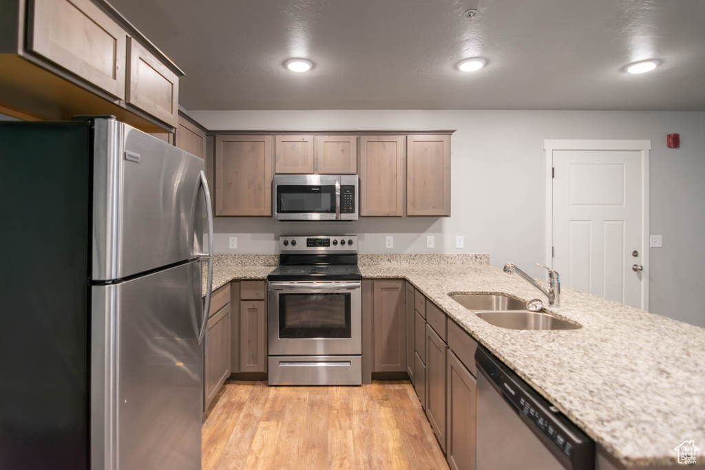 Kitchen featuring appliances with stainless steel finishes, a peninsula, light wood-style floors, light stone counters, and recessed lighting
