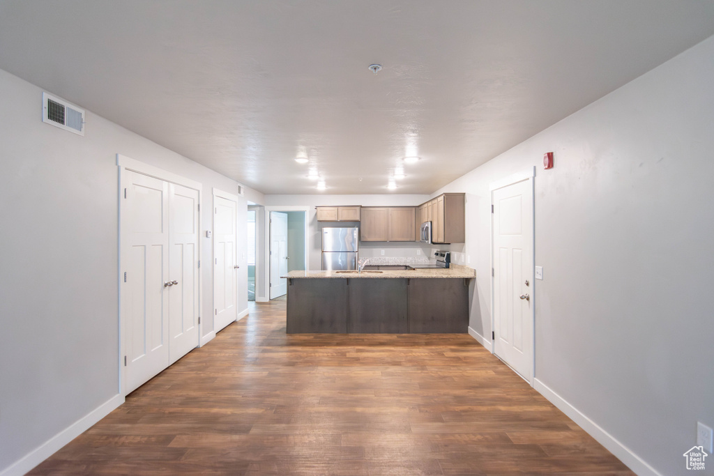 Kitchen featuring appliances with stainless steel finishes, a peninsula, dark wood-type flooring, and light countertops