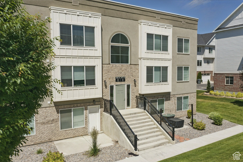 View of front of home featuring stucco siding, a front yard, brick siding, and board and batten siding