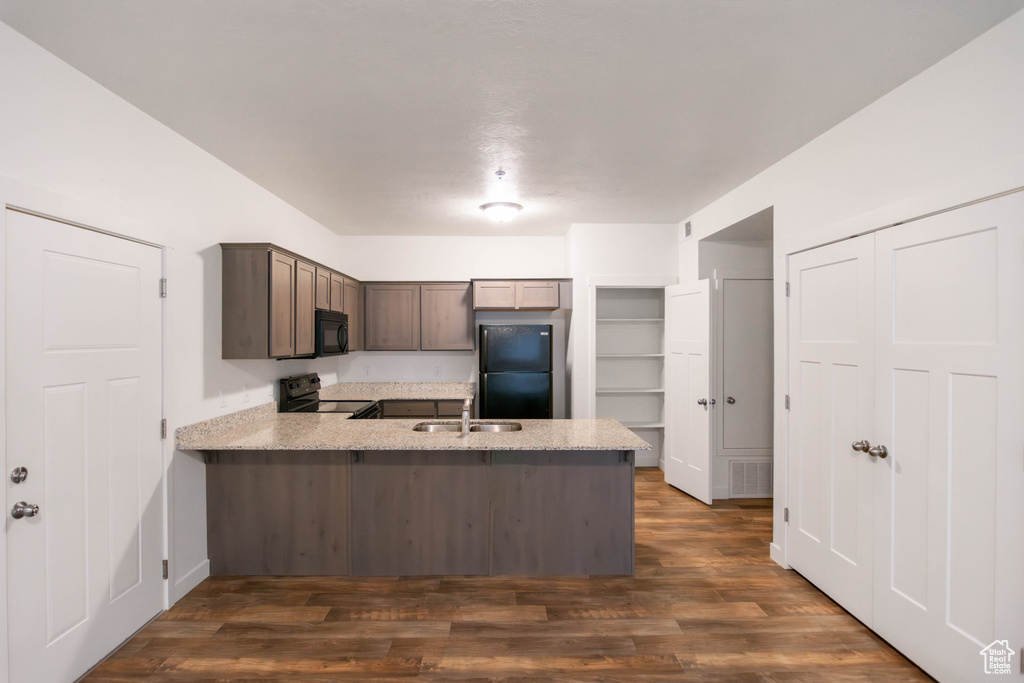 Kitchen featuring black appliances, a peninsula, dark wood-style floors, dark brown cabinetry, and light stone counters